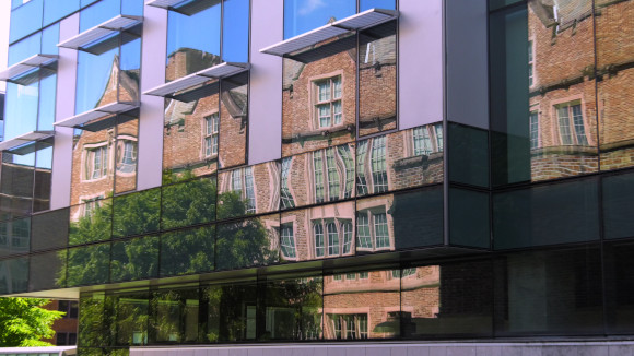 An old brick building reflected in the glass exterior of a modern building