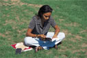 photo of a girl sitting cross-legged on a green lawn, reading a book