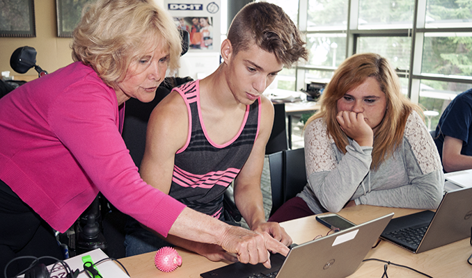 An educator works with two students on a computing project