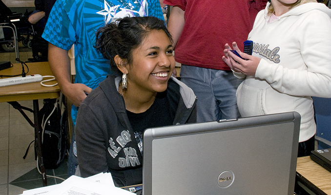 A group of students congregate around a computer