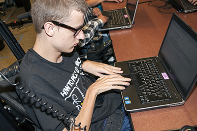 A boy in a wheelchair types on a computer.
