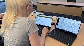 A student uses screen enlarging software and two laptops to work on a coding project.
