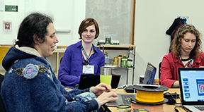 A faculty member with a disability types on a computer while students work in the background.