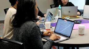 A woman works on a computer at a table with others.