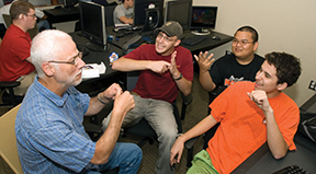 Richard signs with a group of students surrounded by computers.