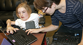 A female mentor working with a female student with a disability on a computer.