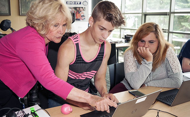 An educator works with two students on a computing project