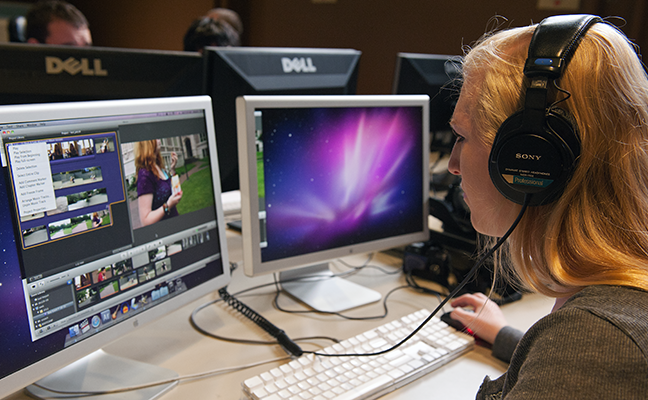 A student using headphones works on video editing on her computer