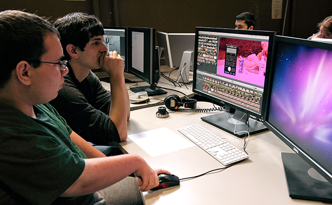 A student with a disability works with an educator to edit a video on a desktop computer