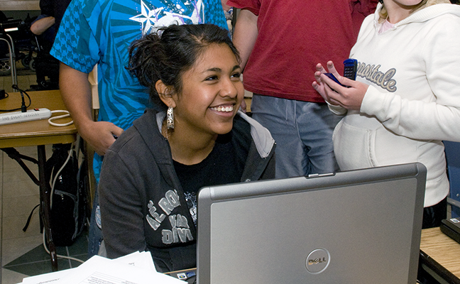 A group of students congregate around a computer