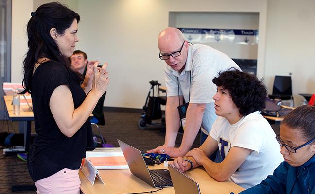 A student looks to an interpreter while the educator shows him how to design a website.