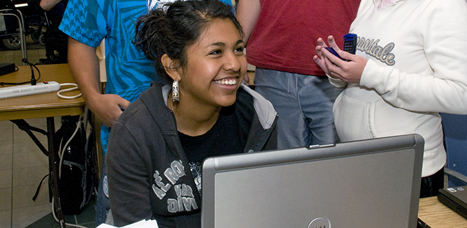 A group of students congregate around a computer