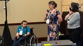 AccessComputing Director Brianna Blaser hosts two speakers with microphones towards the front of a room.