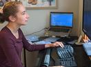 A woman works on a desktop computer in her own office with a laptop beside her.