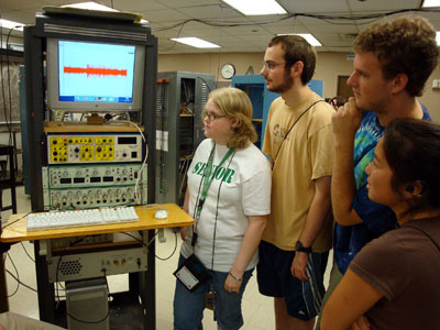 Photo of group of students watching with interest as they gather around a rack of scientific equipment
