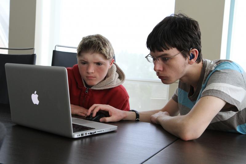 Two students, one with visible hearing aid, use a computer together.