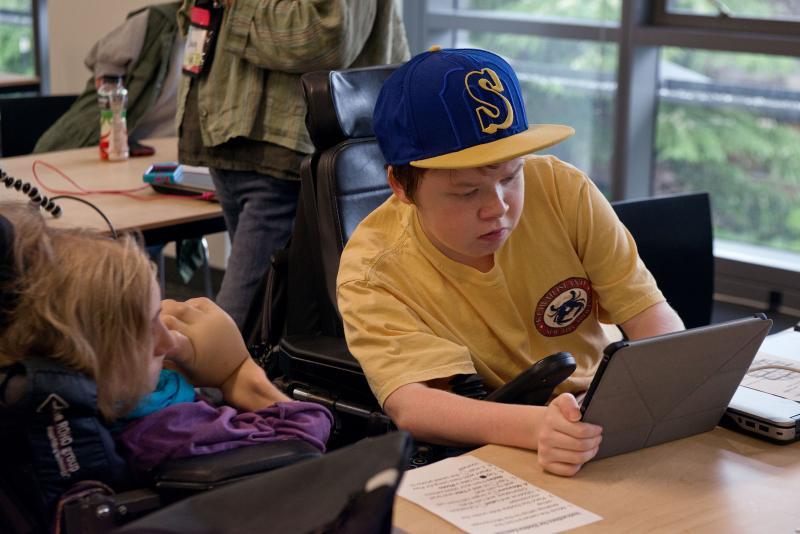 One student holds a tablet while another student looks on.