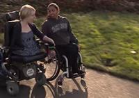 Two students in wheelchairs go down a college path.