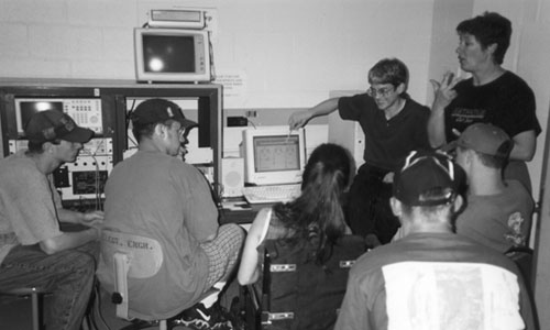 Picture of students working  together at a computer and a sign language interpreter is interpreting.