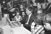 Dean Martineau, DO-IT Mentor, demonstrates a talking computer to school children at the U.W. Computer Fair. Picture of children watching Dean Martineau use laptop computer