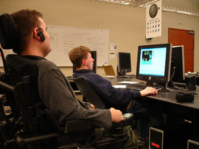 Phase II Scholar Lukas plays the Game of Life as Ambassador Chris offers tips for success. Picture of Lukas at a computer with Chris looking on.