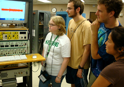 '08 Scholars Brianna, Aaron, and Collin with Intern and '07 Scholar Robyn at the neurobiology workshop during Summer Study. Picture of Brianna, Aaron, and Collin looking at lab equipment.