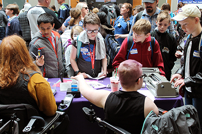 Two staff members demonstrate accessible technology to children.