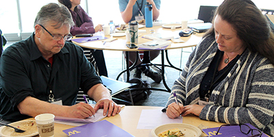 Two participants write down ideas and resources on their feedback forms.