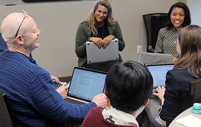 Participants sit around a table with computers and talk to each other.