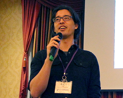 Amy Ko speaks at event, a microphone in hand, and a projector screen behind them. Amy Ko speaks at event, a microphone in hand, and a projector screen behind them.