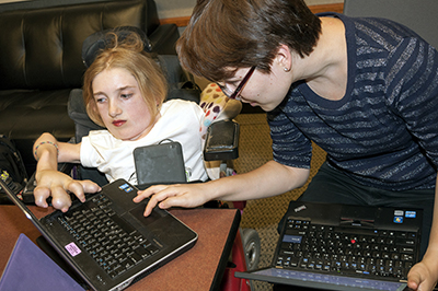 An instructor works with a student in a wheelchair with a laptop.