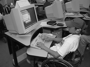 Photo of a student in a wheelchair using a computer at an adjustable table.