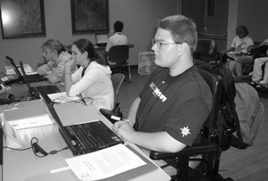 Photo of a student in a wheelchair seated at a computer listening to a lecture.