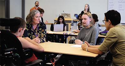 Students and adults sit around a table talking.