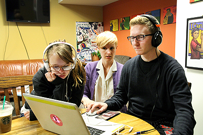 Two students work together on a computer with the help of a mentor.