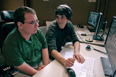 A student in a wheelchair looks at a computer while another student explains something.