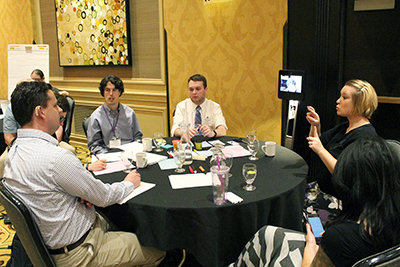 An interpreter signs while one person speaks at a table of people. An interpreter signs while one person speaks at a table of people.