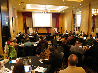 An overview of the event room, showing all of the participants watching a presentation.