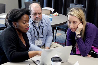 Three participants view resources on a laptop during the AccessEngineering capacity building institute.