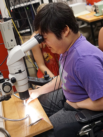 A student in a wheelchair looks into a microscope.