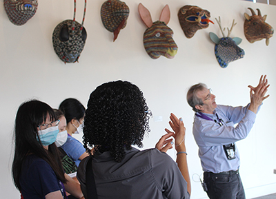 Eric Chudler teaches a group of students in front of a series of masks on the wall. Eric Chudler teaches a group of students in front of a series of masks on the wall.
