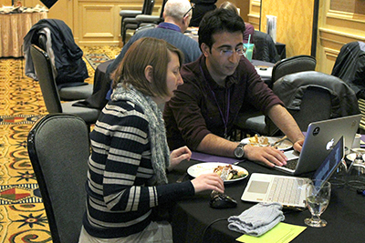 One participant uses a computer while another discusses ideas.