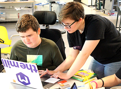 A mentor works with a student in a wheelchair on a computer.