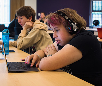 A student wears headphones and works on the computer.