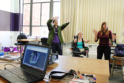 Three students hold up their hands while working with 3D modeling.