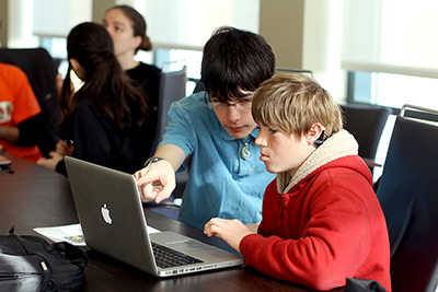 An older student peer-mentors a younger student on a coding project. An older student peer-mentors a younger student on a coding project.