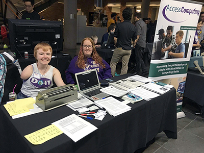 Two scholars man a booth with accessible science equipment and a brailler.