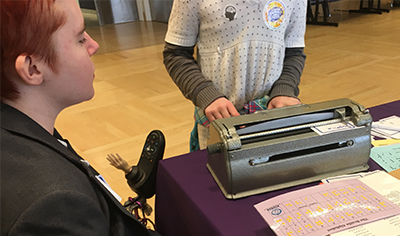 A DO-IT staff member helps a student type out their name using a Perkins Brailler.