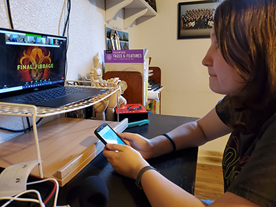 Student working on phone and laptop with raised desktop