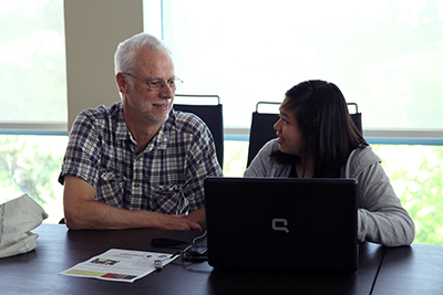 Student working on computer and getting help from older man